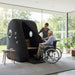 Carer assisting elderly man in a wheelchair into the Henshaw Easy Access Hyperbaric Oxygen Chamber for safe and inclusive wellness treatment.