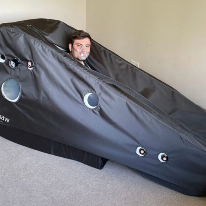 Man inside a Henshaw Recline Hyperbaric Oxygen Chamber using an oxygen mask for wellness and recovery therapy at home.