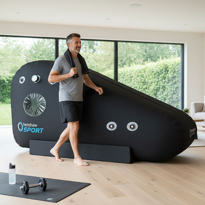 Smiling man post-workout next to the Henshaw Recline XL Sport Hyperbaric Oxygen Chamber in a home wellness space.