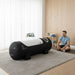 Man relaxing beside the Henshaw Solo Hyperbaric Oxygen Chamber in a minimalist home wellness room, suited for daily recovery routines.