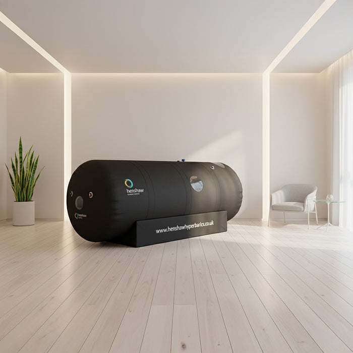 Sleek Henshaw Space Hyperbaric Oxygen Chamber placed in a softly lit minimalist therapy room with indoor plant and armchair.