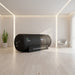 Sleek Henshaw Space Hyperbaric Oxygen Chamber placed in a softly lit minimalist therapy room with indoor plant and armchair.