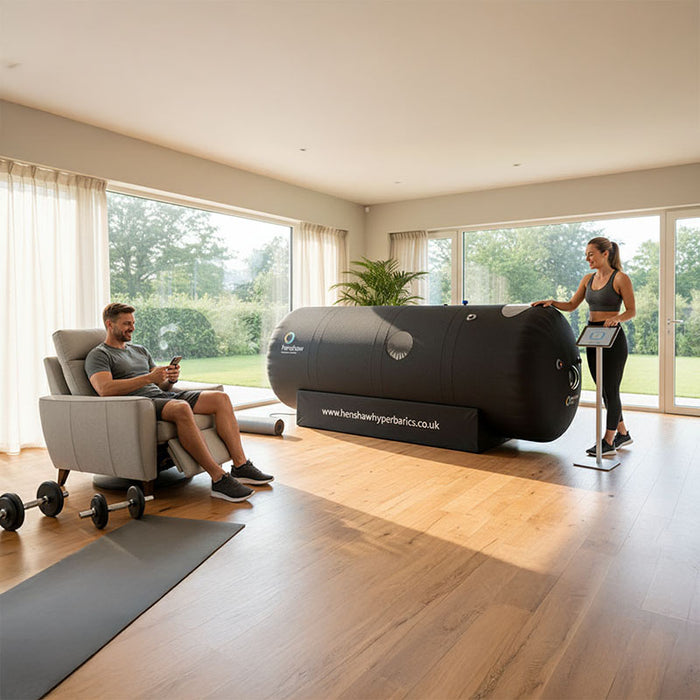 Woman seated inside Henshaw Space Hyperbaric Oxygen Chamber during a session, assisted by a wellness technician in a professional environment.