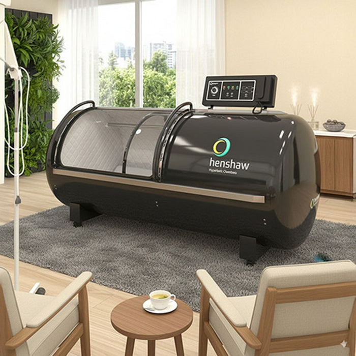 Henshaw XL Pro Hyperbaric Oxygen Chamber situated in a cosy lounge-style therapy room, with IV stand and seating for comfortable and effective treatment sessions.