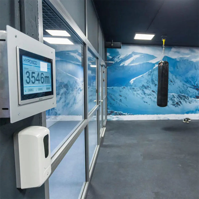 Hypoxico Full Climate Hypoxic Chamber interior with curved treadmill handrail in foreground and branded black entry door with observation window in background.