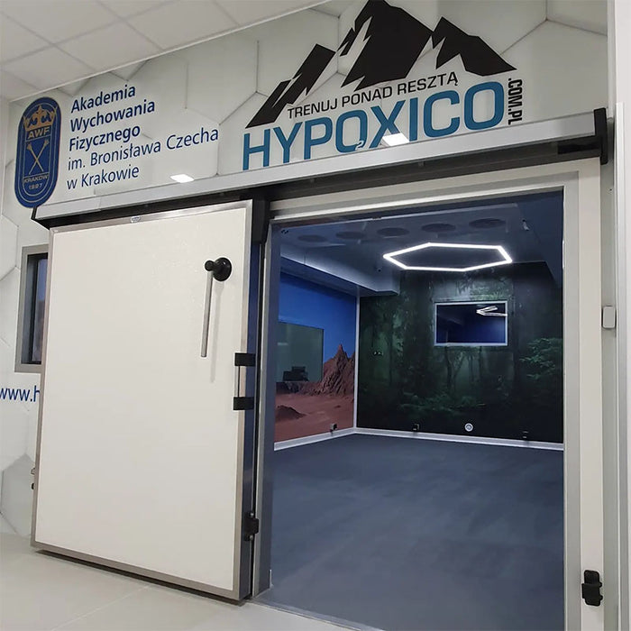 Hypoxico Full Climate Hypoxic Chamber room entry with large insulated sliding door, branded signage above, and mountain landscape mural visible inside.