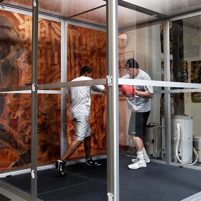 Hypoxico Hypoxic Altitude Chamber acrylic portable pod with aluminium frame in a boxing gym, two athletes sparring inside, boxing posters visible on surrounding walls.