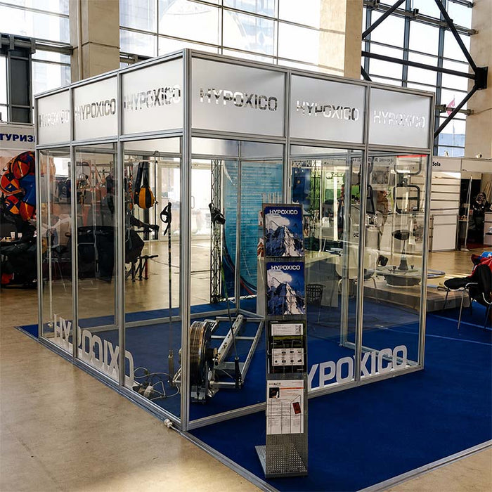 Hypoxico Hypoxic Altitude Chamber large walk-in enclosure with aluminium frame and clear panels in a public leisure centre, elliptical trainer inside and hypoxic generator unit alongside.