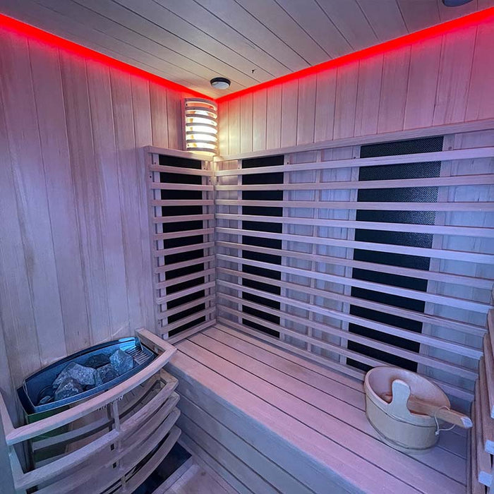 The spacious interior of the Insignia Outdoor Hybrid Infrared Sauna 1700 x 1500mm, featuring a wooden bench, Finnish Harvia stove, and radiant infrared panels, illuminated by red LED Chromotherapy lighting.