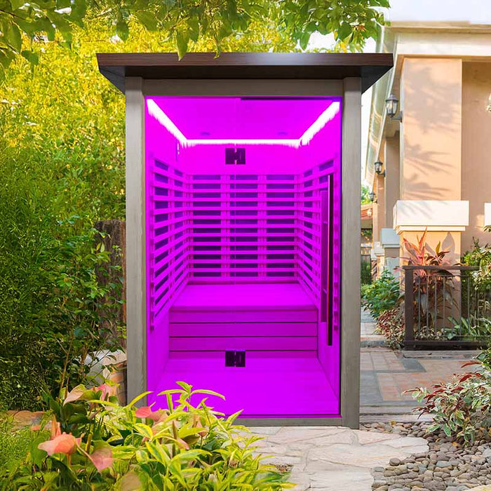 Exterior view of the Insignia Outdoor Infrared Sauna with purple LED lighting, blending into a natural garden setting.