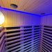 A serene interior of the Insignia Outdoor Infrared Sauna 1500 x 1300mm bathed in blue chromotherapy lighting, featuring the elegant wooden slats and sleek heater panels.