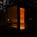 Night-time exterior angle of the Jonas Classic 4-person garden sauna with door open, revealing warm-lit wooden interior.