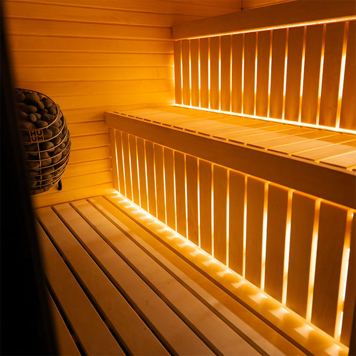 Interior view of the Jonas Classic 4-person outdoor sauna featuring natural timber benches, LED strip lighting, and HUUM stone heater.