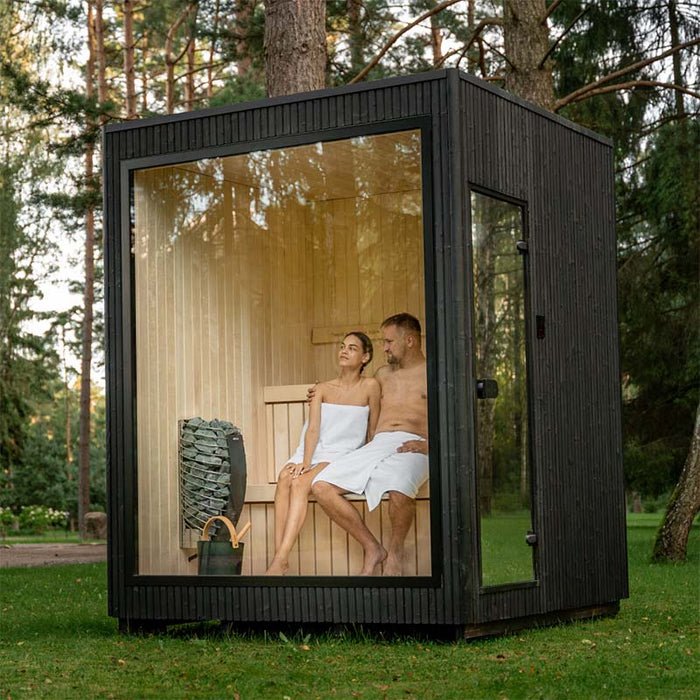 Couple enjoying a serene moment inside the Jonas Classic outdoor sauna, seen through the full-height glass front in a forested setting.