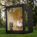 Couple enjoying a serene moment inside the Jonas Classic outdoor sauna, seen through the full-height glass front in a forested setting.