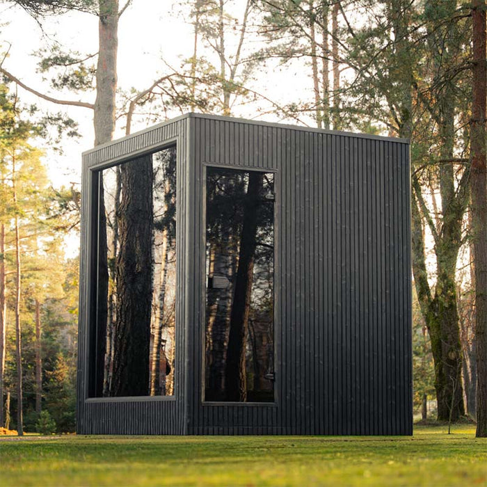 Side profile of the Jonas Classic outdoor sauna set amongst trees, highlighting tall reflective glass panels and clean architectural lines.