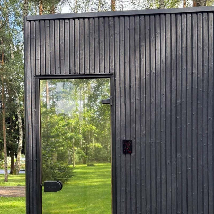 Close-up of Jonas Classic sauna entrance with clear glass door, modern black timber exterior, and control panel on wall.