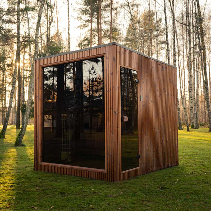 Full exterior shot of the Jonas Grand 8-person outdoor sauna placed on a lush green lawn with tall trees in the background.