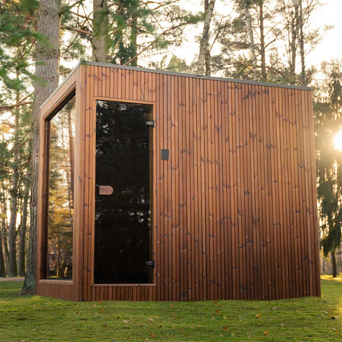 Side view of the Jonas Grand 8-person outdoor sauna at sunset, highlighting its vertical wood cladding and full-height glass door.