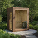 Wooden Jonas Mini 3-person outdoor sauna placed in a lush green garden, blending seamlessly with nature for a peaceful escape.