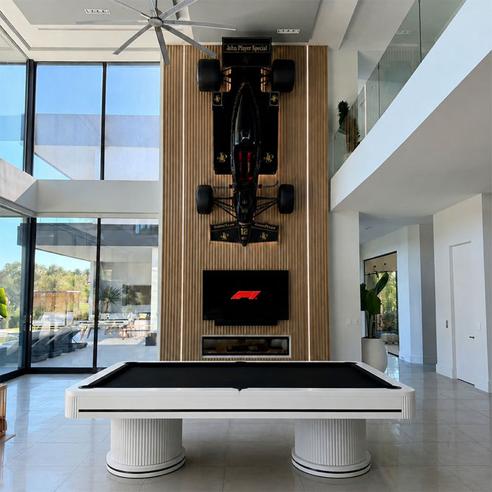 Koralturk Elit luxury billiards table with black cloth, white fluted pedestal legs and metallic detailing in an elegant city-view interior.