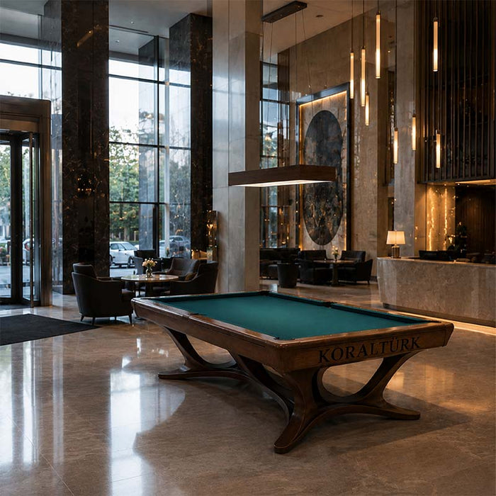 Koralturk Legnora Pool Table with green cloth and sculptural wooden frame displayed in an elegant luxury hotel lobby.
