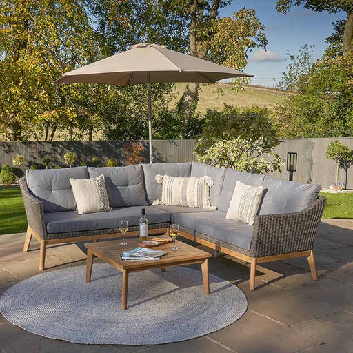 Larissa Outdoor Corner Seating Set arranged in a garden setting with a wooden coffee table and a parasol, showcasing its stylish rattan design and comfortable cushions.