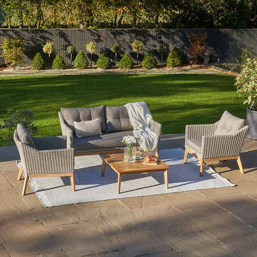 The Larissa Outdoor Seating Set arranged in a lush garden, showcasing the stylish grey cushions and light teak-effect acacia wood frame, perfect for relaxing or entertaining outdoors.