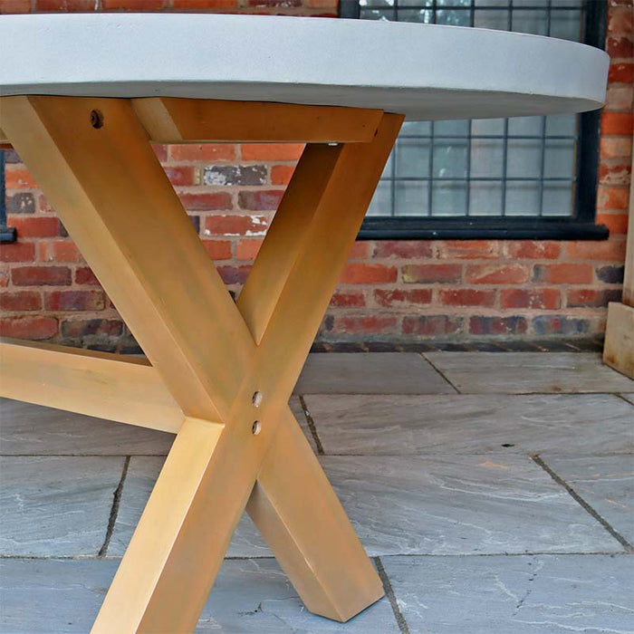 A close-up showing the X-shaped wooden legs of the round concrete table, part of the elegant and durable Luna 6 Seater Concrete Table Dining Set.