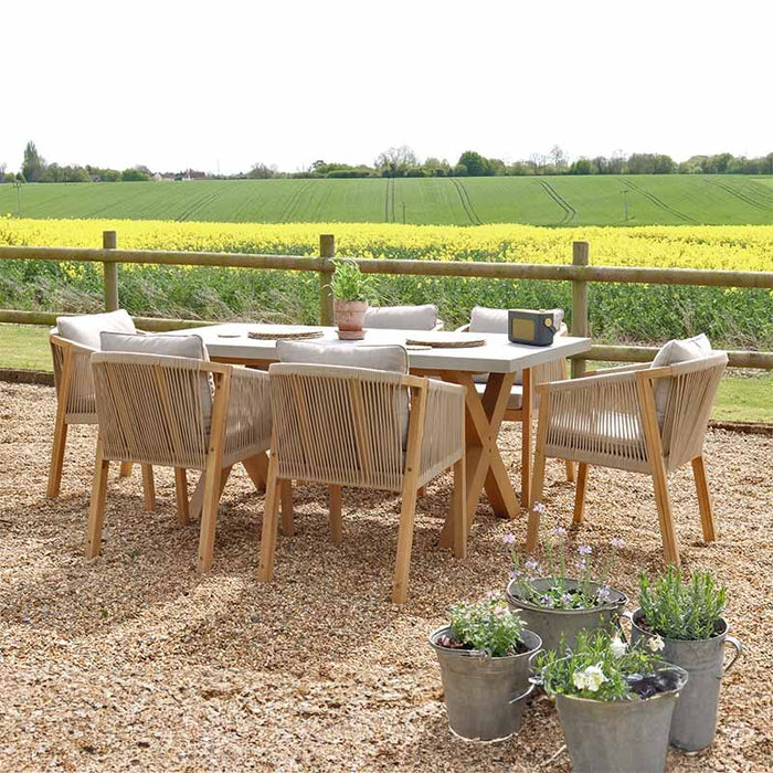 A side profile of the complete Luna dining set with six rope chairs arranged around the concrete table in a scenic outdoor setting.