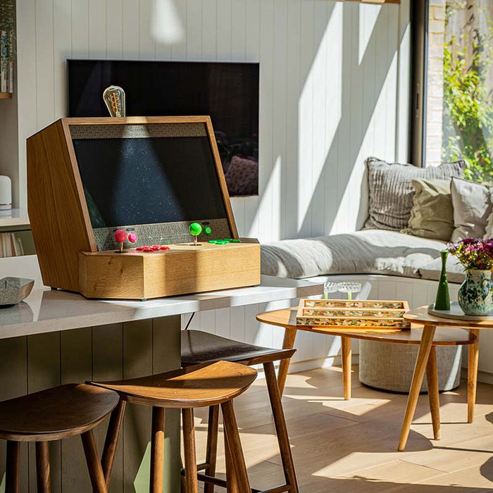 Maison Roshi Sensei V1 arcade cabinet with pink and green controls, placed on a kitchen island in a sunlit modern home interior for stylish retro gaming.