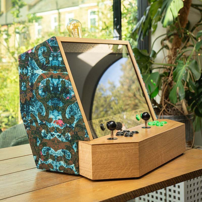 Maison Roshi Sensei V2 arcade cabinet with black and green controls, featuring velvet side panels in a vibrant blue pattern, placed in a bright modern interior.