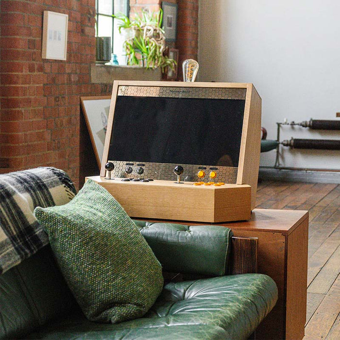 Maison Roshi Sensei V2 wooden arcade cabinet with black and yellow controls, set atop a green leather armrest in a rustic loft-style living space.