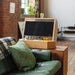 Maison Roshi Sensei V2 wooden arcade cabinet with black and yellow controls, set atop a green leather armrest in a rustic loft-style living space.