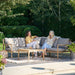 Two women enjoying a conversation on the Malta Outdoor Corner Seating Set in a lush garden setting.