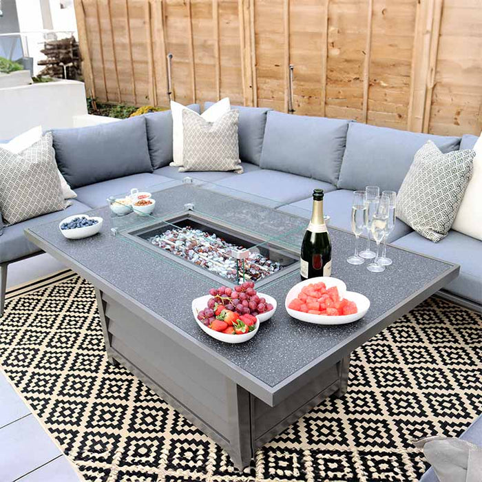 Close-up of the Mayfair Fire Pit Table, set with fruits and champagne, creating a stylish outdoor dining experience.