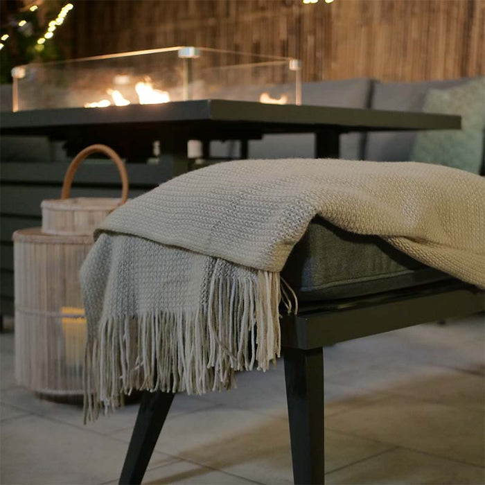 Close-up of the Mayfair bench draped with a cosy blanket, set against the backdrop of a warm fire pit.