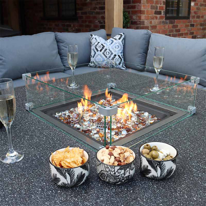 A detailed view of the glowing fire pit from the Mayfair Corner Lounge Set, with glasses and snacks on the table, illustrating the luxurious and cosy feel of this outdoor furniture set.