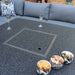 A close-up of the Mayfair Corner Lounge Set fire pit table with its cover in place, surrounded by snacks and drinks, highlighting the versatile design for both dining and entertaining.