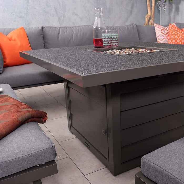 A close-up of the Mayfair Fire Pit Table with its sleek, tempered glass top, complemented by the comfortable grey cushions and vibrant orange pillows on the lounge set.