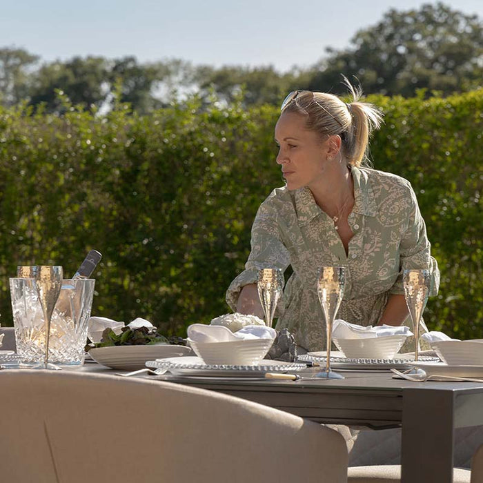 A woman preparing the Ambition 10 seater extending dining set in oatmeal, arranged for a luxurious outdoor dining experience.