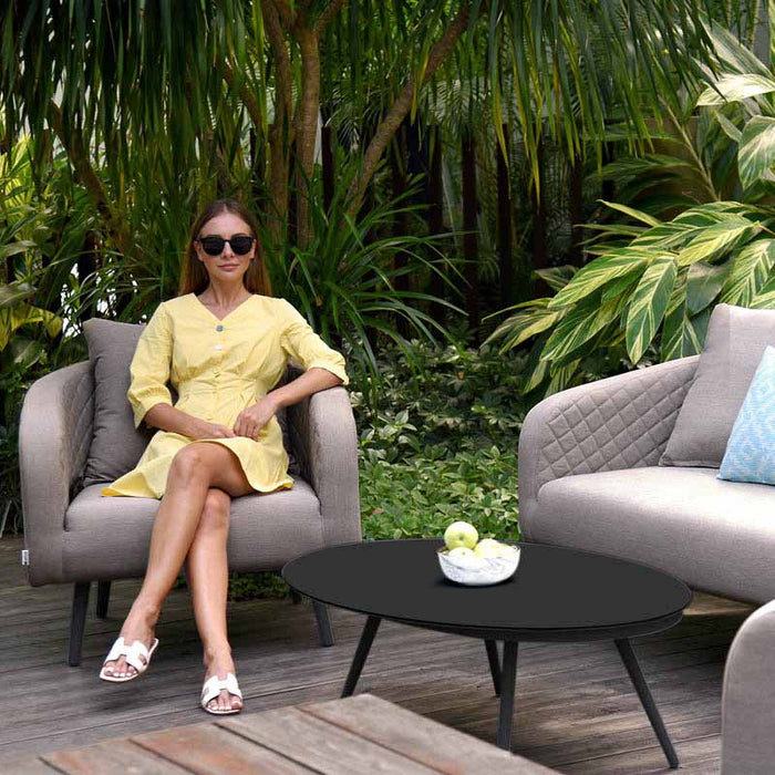 Woman seated on an Ambition armchair, enjoying the Taupe 3 Seater Sofa Set in a garden setting.