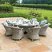 Maze Oxford Heritage 8 Seater Round Dining Set displayed on a patio, complete with grey rattan chairs and a glass-top table, set amidst a scenic garden.