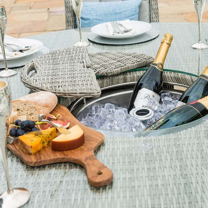 Close-up of the Maze Oxford Heritage dining table's integrated ice bucket filled with ice and champagne, detailed with a rattan lid, set amidst a luxurious outdoor dining arrangement.