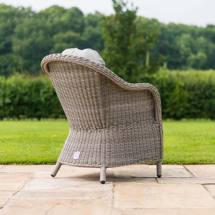 Rear view of a grey rattan dining chair from the Maze Oxford Heritage 8 Seater Round Dining Set, elegantly designed with a curved back and plush grey cushion, positioned on a patio with a lush green garden in the background.