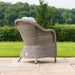 Rear view of a grey rattan dining chair from the Maze Oxford Heritage 8 Seater Round Dining Set, elegantly designed with a curved back and plush grey cushion, positioned on a patio with a lush green garden in the background.