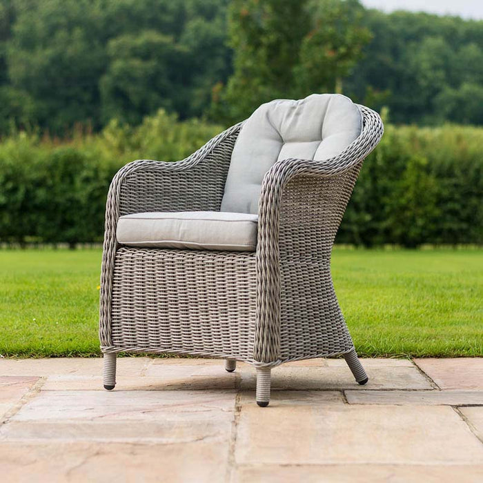 Elegant grey rattan chair from the Maze Oxford Heritage 8 Seater Round Dining Set, showcasing plush grey cushioning and a detailed weave design, set against a lush green garden backdrop.