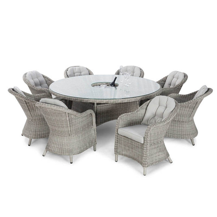 Angled view of the Maze Oxford Heritage dining table with a rattan chair, showcasing the table's glass top and the chair's detailed weave in a garden setting.