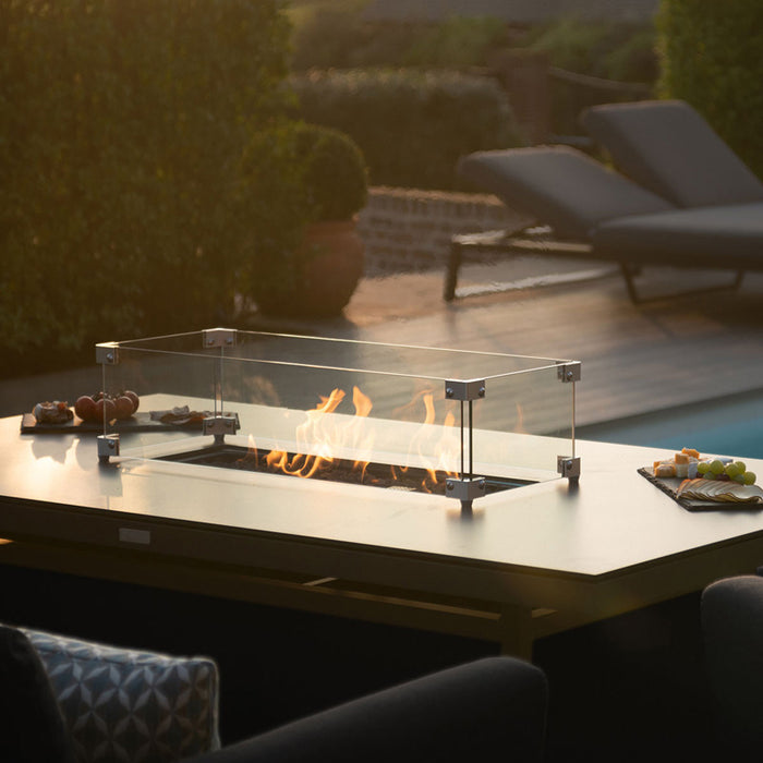 Close-up of the Pulse 3 Seater Sofa Dining Set with glass fire pit guard in a charcoal finish, set beside an outdoor pool with snacks on the table.