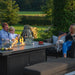 Family enjoying a cosy evening around the Pulse 3 Seater Sofa Dining Set with Fire Pit, featuring a charcoal finish, comfortable seating, and glowing flames creating a warm ambience.